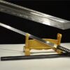 A black Chokuto sword leaning against a wooden stand, with its black scabbard on the floor below and a close-up of its blade tip above.