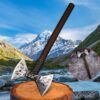 A small, double sided battle axe displayed against a wood log and a mountain wilderness background.