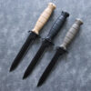 Three combat army daggers with different color handles and black blades lying on the floor.