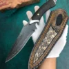 A hand with white glove holding a Damascus wilderness bush knife and leather sheath.