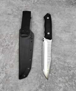 A fixed blade survival knife with a black handle and silver blade next to its black Kydex material sheath, lying on a grey concrete floor.