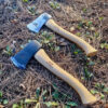 Two small camp axes displayed lying side-by-side on a forest floor.