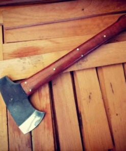 A full tang camp tomahawk with a wood handle, displayed lying on a wooden floor.