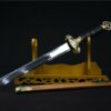 A straight, double edged Chinese short sword leaning against a wooden stand, with its scabbard below on the floor.