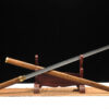 A Japanese Chokuto Katana sword, displayed crossed against its wooden scabbard, leaning against a small sword-stand.