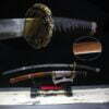 A curved sword Tachi displayed next to its scabbard, on a small wooden sword-stand.