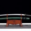 A folded, Damascus steel Katana, displayed next to its green scabbard, on a small wooden sword-stand.