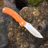 Folding hunting knife with blade opened lying on a rock.