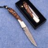 Two gentlemans pocket knives; one with blade opened lying on blue carpet, and the other in a closed position within a small black box.