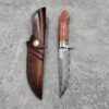 Hunting Knife with leather sheath lying on a grey concrete floor.