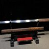 A Wakizashi Japanese short sword, displayed next to its wood scabbard, on a small wooden sword-stand.