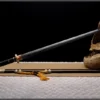 A Jian sword with a straight, double edged blade displayed leaning against a small wood log, along with its decorative scabbard lying below on the floor.