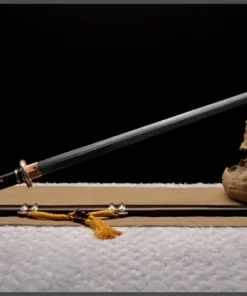 A Jian sword with a straight, double edged blade displayed leaning against a small wood log, along with its decorative scabbard lying below on the floor.
