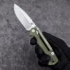 A hand with black glove holding a survival military folding knife with army green color handle.