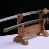 A WW2 military sword Katana displayed on a small wooden stand, next to its army green scabbard.