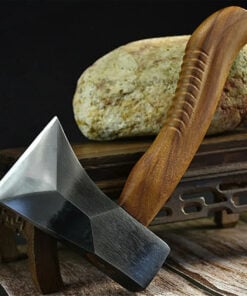 A mini hatchet with a wooden handle, leaning against a small table, with a rock on-top of the table.