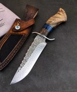 A wood handle fixed blade knife with a Damascus steel blade and its leather sheath lying on a concrete floor.