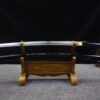 A Shirasaya sword and its black scabbard displayed on a small wooden stand.