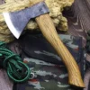 A one handed axe with a wooden handle, lying on a small camouflage bag, next to green rope on a wooden floor.