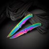Two rainbow colored pocket knives leaning against green paracord rope.