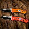 Two folding rescue knives with different color handles lying on a log.