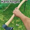 A mans arm holding a small forest axe with a wooden handle against a green grass background.