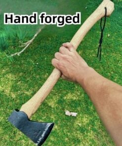 A mans arm holding a small forest axe with a wooden handle against a green grass background.