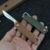 A hand holding two folding mini razor blade knives; one with blade opened and the other in a fully closed position.