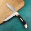 A dual blade folding stockman knife lying againsy a chopping board.