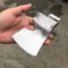 A hand holding a survival axe head against a concrete floor background.