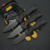 Three black tactical folding knives lying on a work glove, against black floor material.