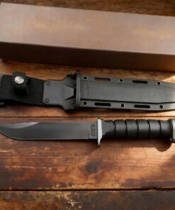 A black colored tactical survival knife, displayed next to its Kydex sheath and box, on a wooden floor.