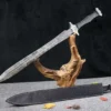 A modern tactical sword displayed on a small wood log, with its scabbard below on the floor.