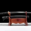 A Japanese short Wakizashi sword and its black scabbard displayed on a wood stand.