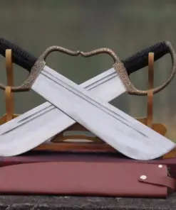 A pair of Win Chun swords with blades crossed, displayed on a small wooden stand, with a leather knife sheath below on the floor.
