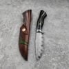 A wood handle fixed blade knife with leather sheath lying together on a grey concrete floor.