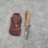 A folding wood handle pocket knife next to its leather pouch, lying on a gret concrete floor.