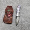 A Damascus folding purple pocket knife with leather sheath.