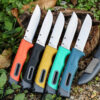 Five fixed blade bushcraft knives lying on forest floor.