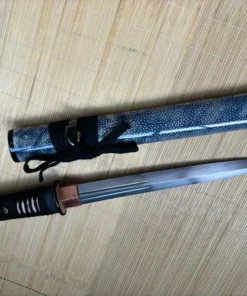A custom Tanto knife, displayed next to its sheath, on a bamboo-mat floor.