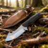 A field dressing gut hook knife displayed next to its sheath, lying on a forest floor.