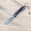 A folding Damascus steel lock blade knife resting on straw matting.