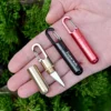 A man's hand holding three mini keychain knife models of differing colors.