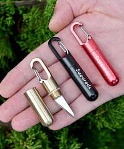 A man's hand holding three mini keychain knife models of differing colors.