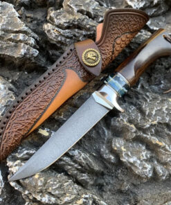 A pig sticker knife displayed next to its leather sheath, lying against rock.