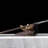 A battle ready spear leaning against a small wood log, with its scabbard below on the floor.