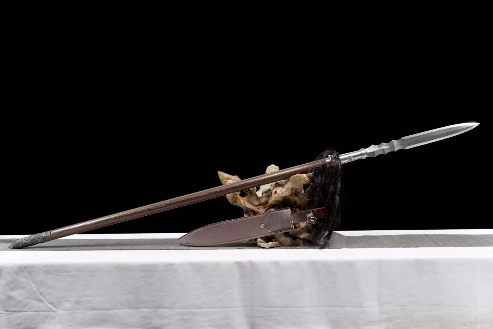 Battle Ready Spear A battle ready spear leaning against a small wood log, with its scabbard below on the floor.