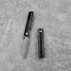 Two folding camping knives lying on a concrete floor; one with its blade opened and the other in a closed position.