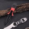 Two dive knives, one black & red in color resting against a small tree branch and the other silver in color lying on the floor.