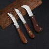 Three folding mushrooming knives resting against a piece of wood.
